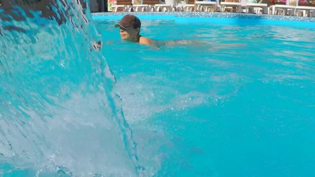 The girl is swimming in the pool. Girl under the streams of a waterfall in the pool.
