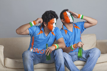 Disappointed young male friends holding bottle while sitting on sofa 
