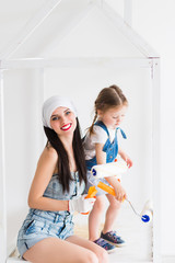 The young smiling woman with her little daughter in the room, they keep platen for painting of crib