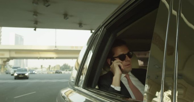 Wealthy man talks on phone next to open window of limo, slow motion