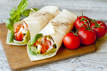 Healthy lunch snack. Tortilla wraps with grilled chicken fillet and fresh vegetables on wooden background. close-up
