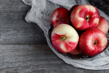 Flat peaches on a metal plate on wooden background. Rustic selective focus.