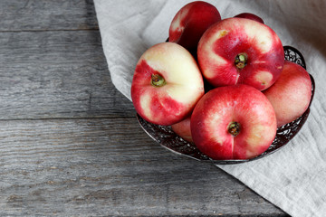 Flat peaches on a metal plate on wooden background. Rustic selective focus.
