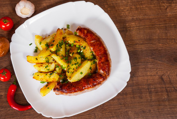 grilled meat sausages with fried potatoes in a plate on wooden table. with copy space. top view