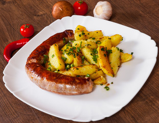 grilled meat sausages with fried potatoes in a plate on wooden table