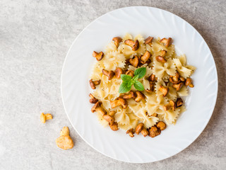 Farfalle pasta with chanterelles and basil on gray stone background
