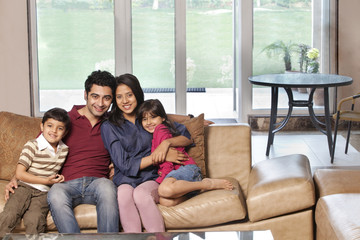 Obraz premium Portrait of happy young parents sitting with children on sofa at home 
