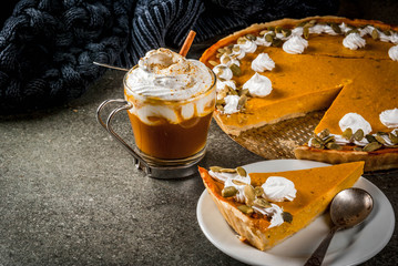 Traditional autumn dishes. Halloween, Thanksgiving. Spicy pumpkin pie with whipped cream & pumpkin seeds, pumpkin latte with cinnamon on black stone table with blanket. Copy space