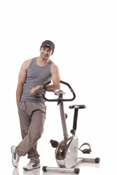 Full length of a young man standing next to an exercise bike over white background 