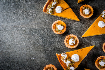 Traditional autumn dishes. Halloween, Thanksgiving. Set of spicy pumpkin pie and pumpkin tartlets with whipped cream & pumpkin seeds on black stone table. top view