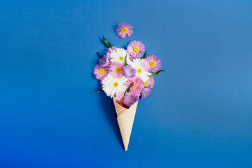 Waffle cone with chamomile flower bouquet on blue background. Flat lay, top view floral background.