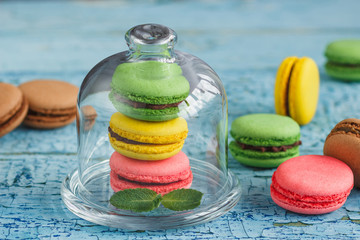 Green, pink and yellow french macarons under the glass on the wooden boards