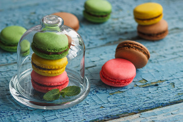 Green, pink and yellow french macarons under the glass on the wooden boards