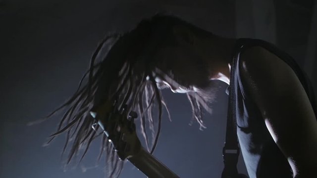 Guitarist rocker with dreadlocks playing the electric guitar on stage. Performance music video rock, punk, heavy metal band in slow motion.