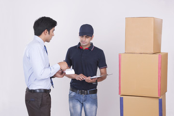 Businessman conversing with delivery man by stacked packages against gray background