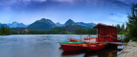 Panoramic picture of beautiful mountain lake Strbske Pleso at summer evening. Moored boats on pier. High Tatras. Slovakia.