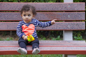 Full length of innocent girl with toy pointing sideways while sitting on park bench