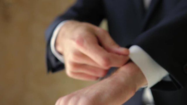 A young man in black suit adjusts his cufflinks of white shirt. Indoor. Close-up. Interior. Sunshine. Steady