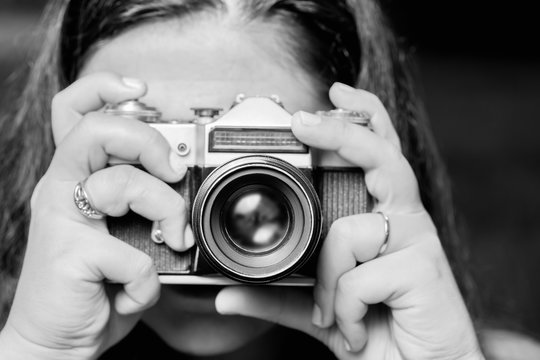 Portrait of young woman taking photos with vintage retro camera. Black and white
