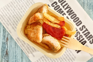 Tasty fried fish and chips in packaging on wooden background