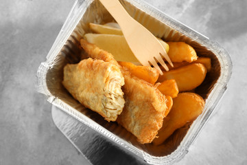 Foil container with tasty fried fish and chips on table