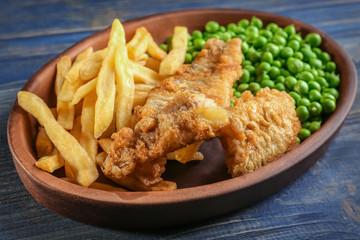 Plate of tasty fried fish and chips with peas on wooden background