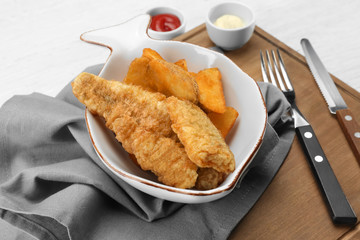 Plate with fried fish and chips on wooden board