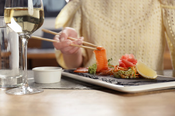Woman holding delicious salmon slice with chopsticks at table