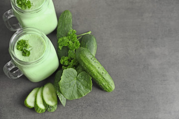 Mason jars with fresh smoothie and cucumbers on grey background