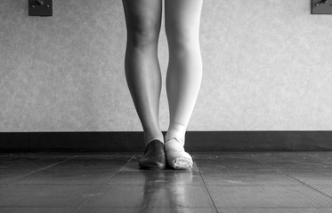 Black and white version of Dancer standing in parallel position at the barre, half dressed in Jazz dance attire and half in ballet attire