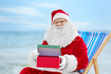 Authentic Santa Claus with gift box in deck chair on beach