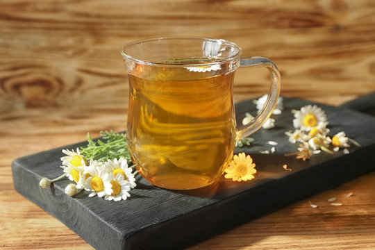 Cup of chamomile tea and board on wooden background