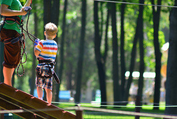 The coach coaches the child to climb in a rope park.