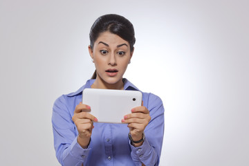 Shocked businesswoman using digital tablet over gray background