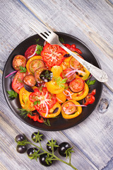 Different sorts of tomatoes, parsley, dill and red onion salad. View from above, top studio shot
