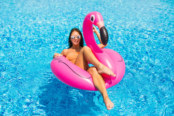 Tan girl sits on inflatable mattress flamingos and relax in the pool. Pool party