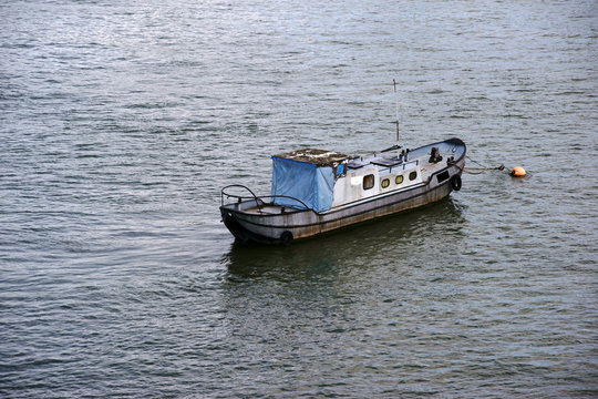 Der alte Kahn  / Ein altes Boot mit verrosteten Seitenwänden und einer zugedeckten Kajüte ankert am Ufer eines Flusses.