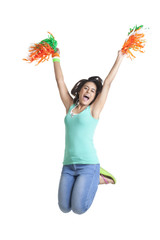 Excited young woman jumping in mid-air while holding pom poms over white background 