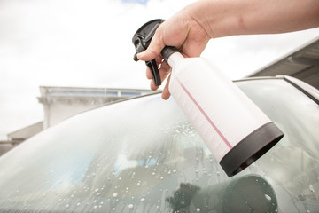 Mann benutzt Sprühflasche zum Scheibenreinigen am Auto