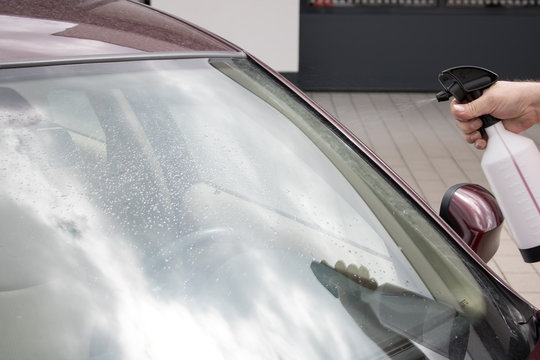 Mann benutzt Spr&uuml;hflasche zum Scheibenreinigen am Auto