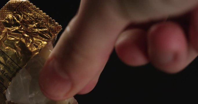 Person unwraps condom from wrapper, close up
