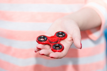 A girl is holding a popular toy metallic red fidget spinner in her hands. Stress relief. Anti stress and relaxation fidgets, spinner for tired people. Girl playing with a fidget spinner.