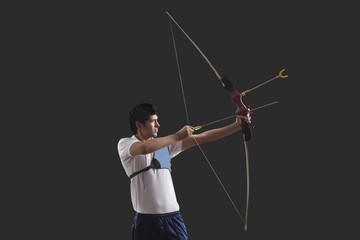 Obraz premium Male archer aiming against black background