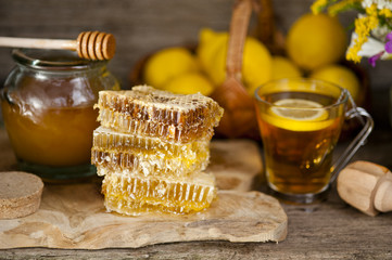 Honey in honeycombs and a barrel of honey or a wooden stick, tea with honey and lemon on a wooden background