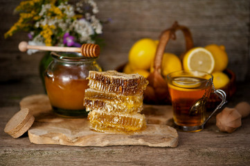 Obraz na płótnie Canvas Honey in honeycombs and a barrel of honey or a wooden stick, tea with honey and lemon on a wooden background