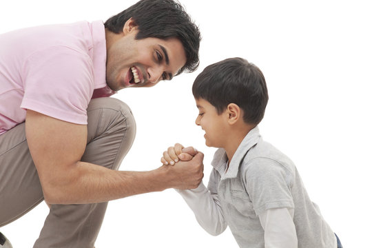Cheerful father and son arm wrestling over white background 