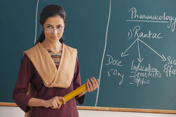 Portrait of young female teacher with attitude holding ruler against chalkboard 