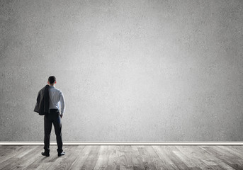 Businessman threw his jacket over his back and looking at blank concrete wall