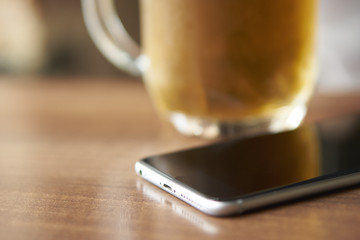 Close-up of a phone lying on a wooden table next to a cup of beer