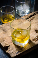 Glass of whiskey with ice placed on wooden planks in vintage style.